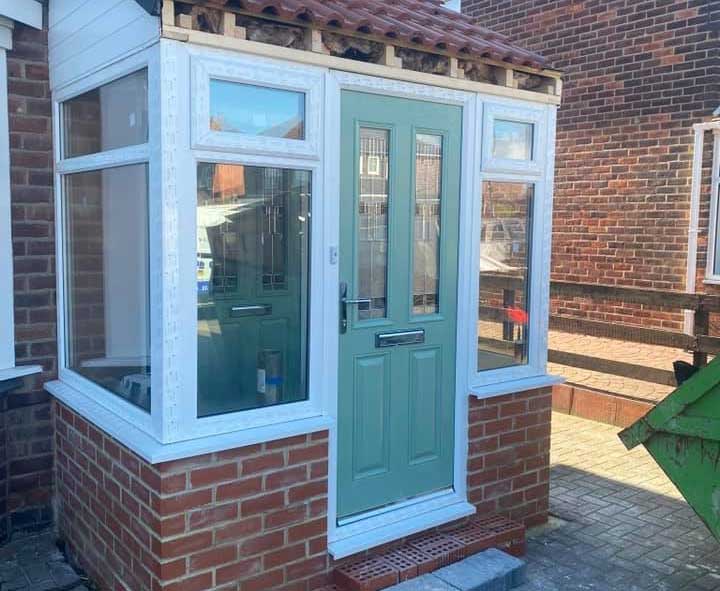 A newly built brick porch under construction with a green front door and tiled roof.