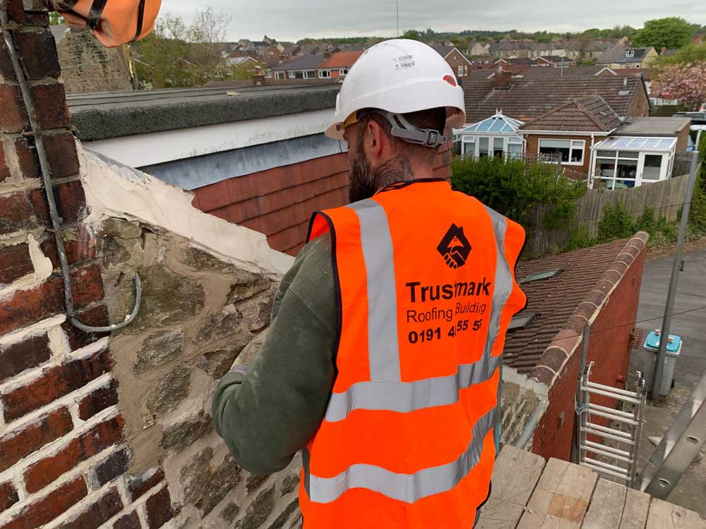 Trustmark Roofing and Building team member repointing brick and stone wall in Northumberland during roofline maintenance