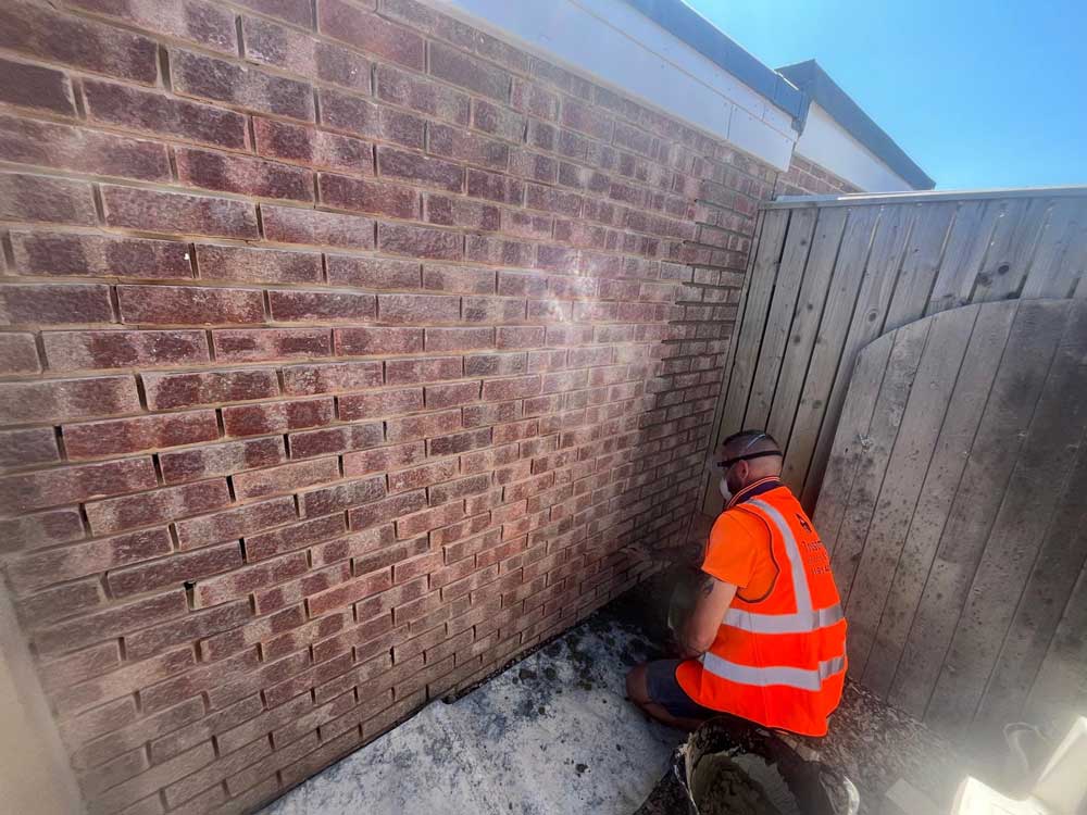 Man kneeling while applying mortar to brick wall in back yard